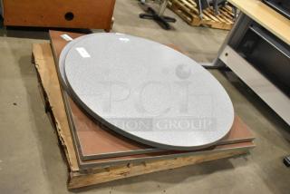 Five tabletops, various shapes and colors, including round and square. Each tabletop is stacked and labeled for bidding.