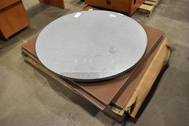 Five assorted tabletops, including round and square shapes, stacked on a pallet. Various wood and laminate finishes, in good condition.