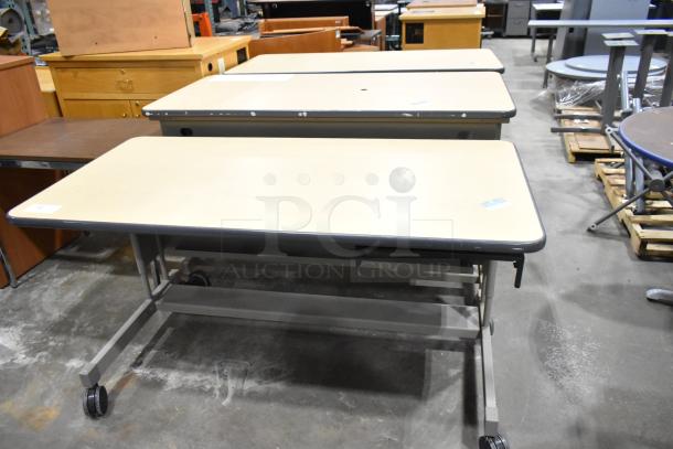Three mobile desks on casters with beige tops and gray frames, in good condition. Auction includes all three units.