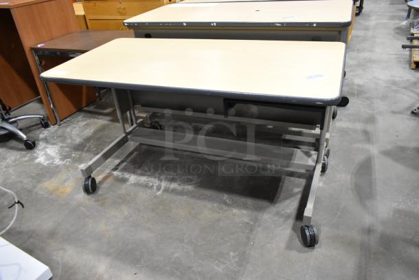 Three rolling desks on casters, beige tops, metal frames, minor wear; versatile for office or classroom use.