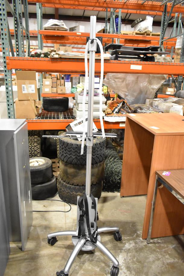 Portable stand on casters, silver finish, adjustable height, tripod base, used condition, ideal for equipment mobility.