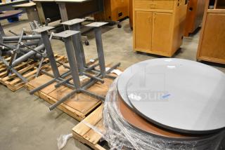 3 pallets of round gray tabletops and gray metal table legs. Items in good condition with visible packing tags.