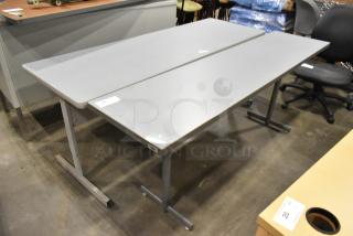 Three gray desks with metal legs and smooth surfaces displayed in a warehouse setting; price tag shown.