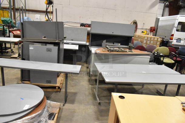 Three gray desks in varied styles, stacked. Some disassembly visible, suitable for office use. Sold as a lot, condition fair.