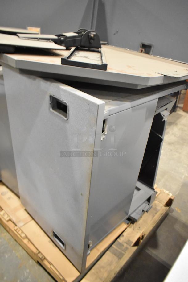 Gray desk set up, featuring a metal cabinet and tabletop with scratches. Appears disassembled on a wooden pallet.