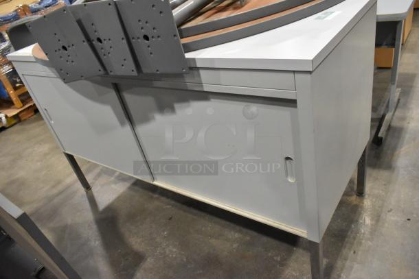 Metal two-door cabinet and tabletop with legs, gray finish, used condition, visible mounts on top, suited for storage or workshop use.