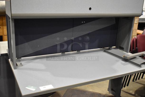 Gray desk with overhead cabinet in good condition, featuring a spacious work surface and integrated storage; auction tag visible.