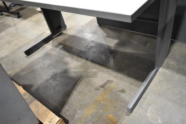 Gray desk with sturdy legs, minimalistic design, showing slight wear. Ideal for office use or home workspace.