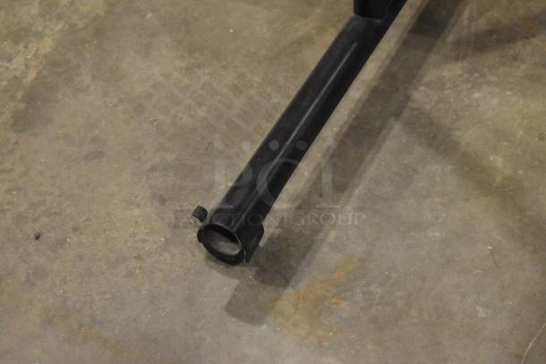 Black metal leg of a desk or table on a concrete floor, part of a set of 4 various desks/tables. Condition appears used.