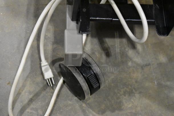 Close-up of black caster wheel with attached white electrical cords on a gray surface.