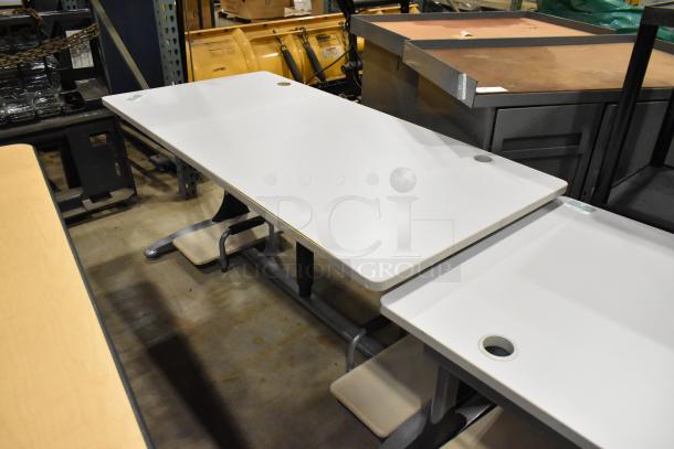 Four various office desks/tables with white laminate tops, metal legs, and cable grommets, stored in a warehouse.