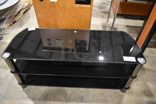Black television stand with two under shelves, glass top, metal legs, excellent condition, small label with number 29.
