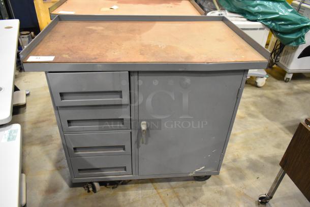 Gray metal cart with four drawers and a door, mounted on commercial casters. Features minor wear.