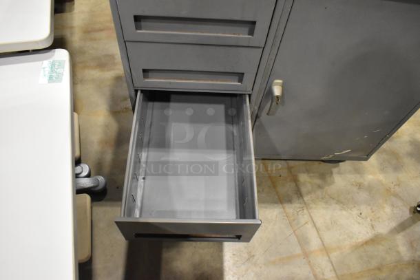 Gray metal cart with four drawers and door, on commercial casters. One drawer open, showing clean interior. Good condition.