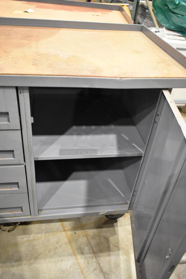 Gray metal cart with four drawers and a door, featuring commercial casters. Interior shelf visible, showing minor wear.