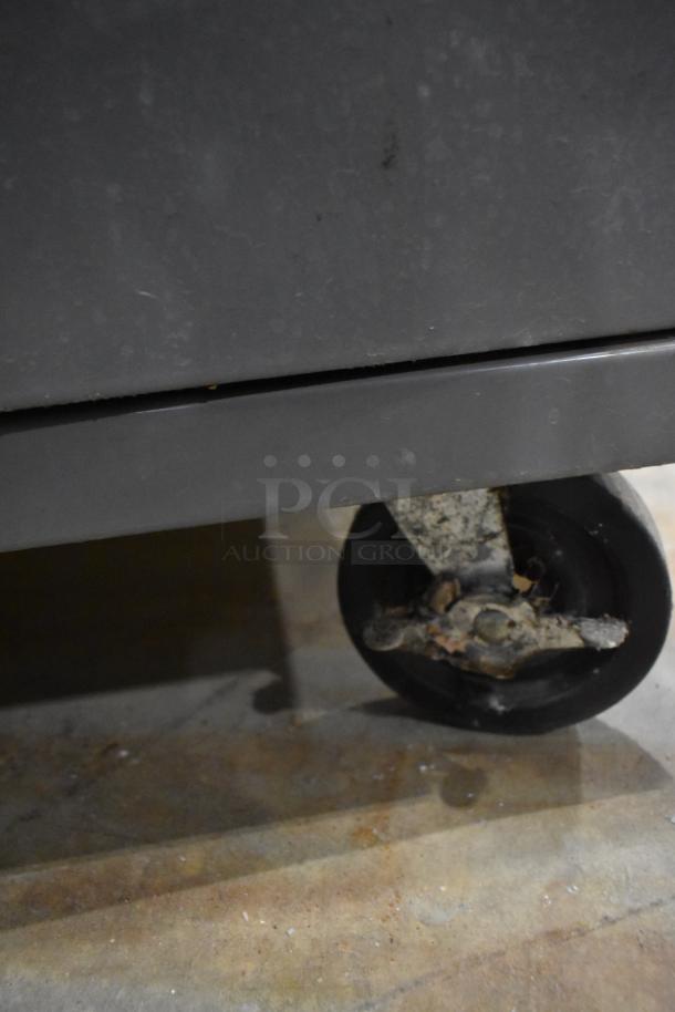 Gray metal cart with four drawers and a door, featuring commercial casters for mobility. Visible wear on the wheels.