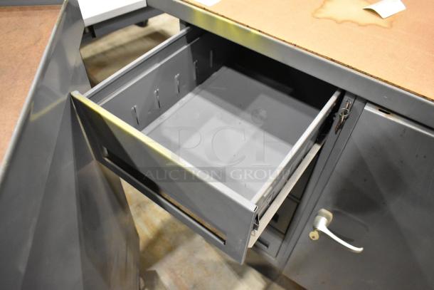 Gray metal cart with four drawers and door, commercial casters, visible wear, open drawer, sturdy industrial design.