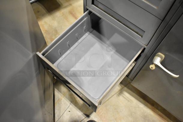 Gray metal cart with open drawer and door, featuring four drawers, commercial casters, and a durable design.
