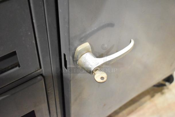 Gray metal cart with 4 drawers and a locking door on commercial casters; visible key in lock.
