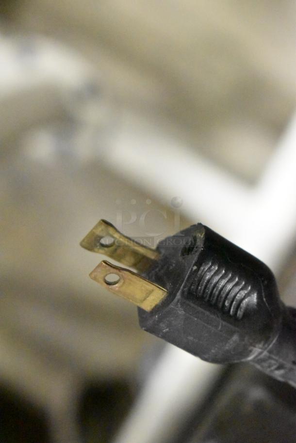 A close-up of a two-prong electrical plug against a blurred background.