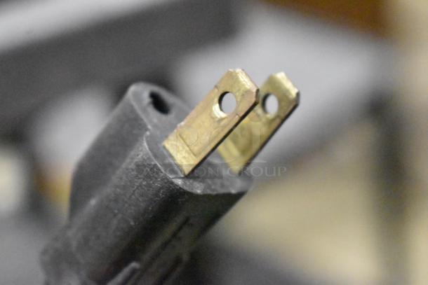 A close-up of a black electrical plug with two brass prongs.