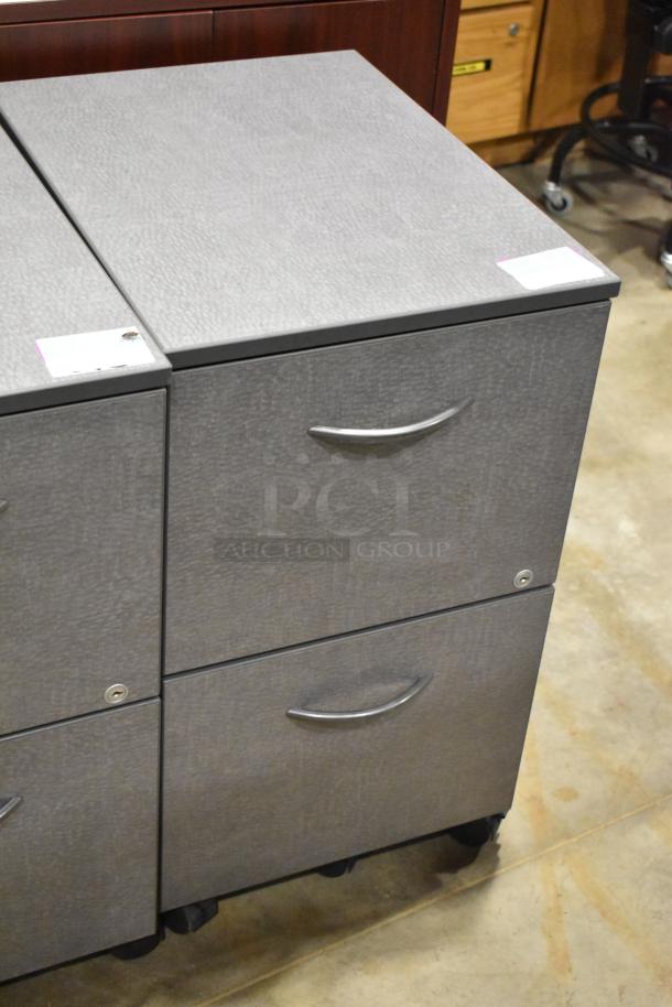 Gray 2-drawer filing cabinet on casters with metal handles; part of auction lot with wood pattern cabinet. Condition: good.