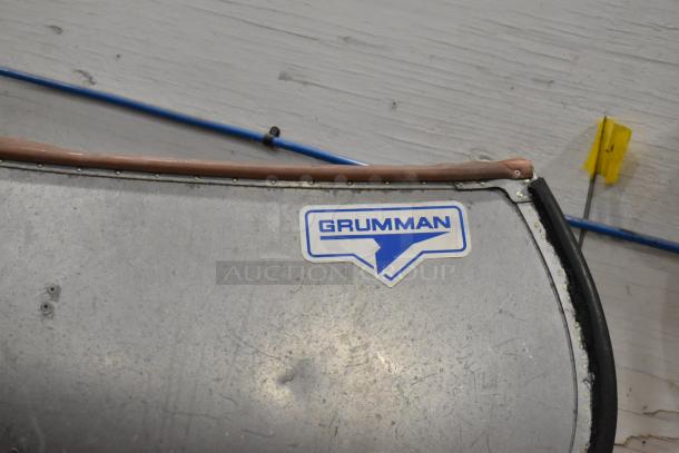 Grumman 13 CANOE metal canoe, 12', with oar and life jacket. Features Grumman logo. Minor wear visible.