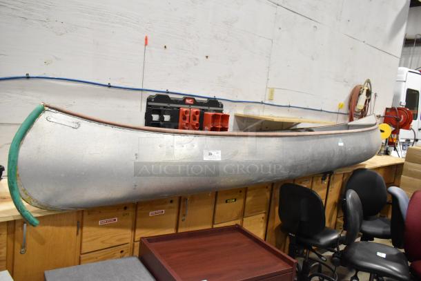 Grumman 12' metal canoe, model 13 CANOE, includes oar and life jacket. Good condition with visible identification tag.