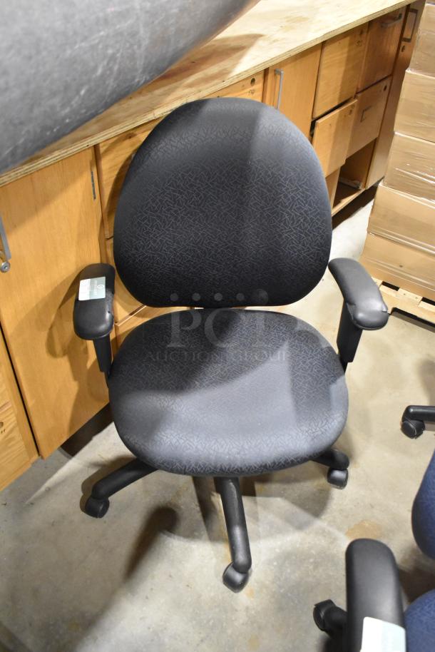 Black office chair on casters, fabric upholstery, adjustable armrests. Slight wear visible. Part of a lot of 10 chairs.