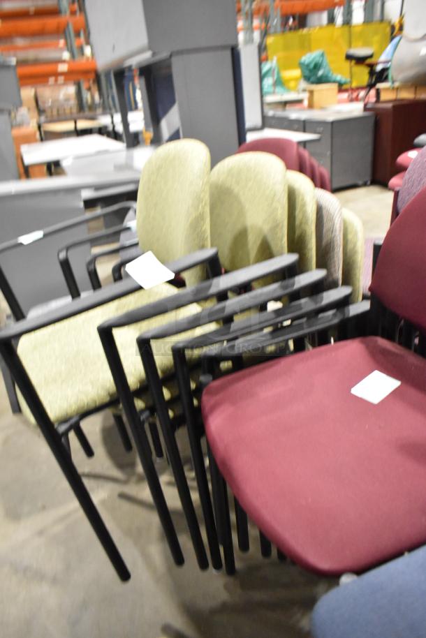 28 assorted chairs, stackable with armrests, mixed colors and fabric, pre-owned condition, labels visible on seats.