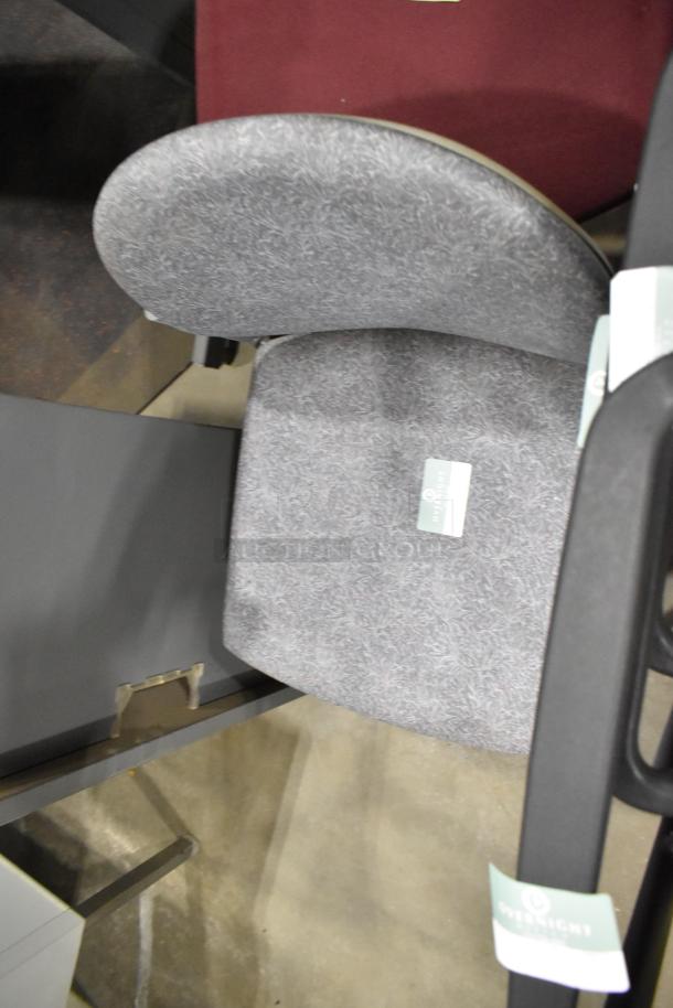 Gray upholstered chair in good condition with armrests, seen among 28 various chairs. Overlight tag visible.