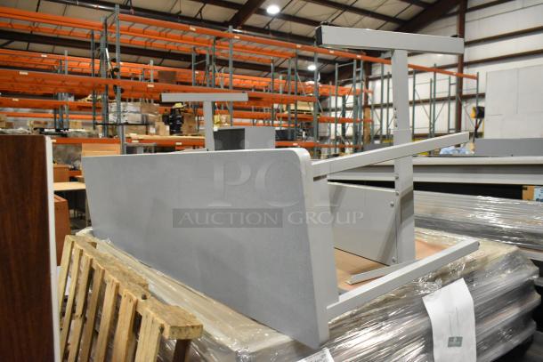 Stack of 23 gray items in a warehouse, including a desk and 22 folding tables. Tables are wrapped in plastic for shipment.