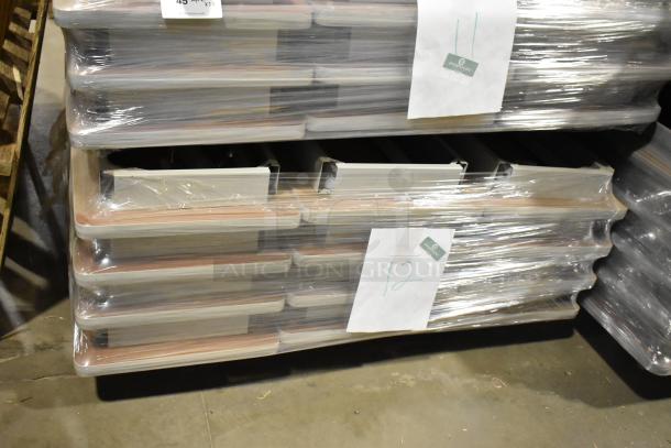 Stack of 23 gray items, including a desk and 22 folding tables. Wrapped in plastic with auction labels indicating lot numbers.