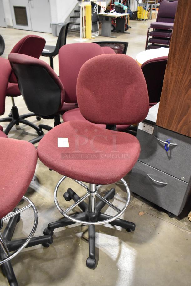 Set of 12 various burgundy chairs, some with casters, in used condition. Adjustable height, metal footrests, ideal for office use.