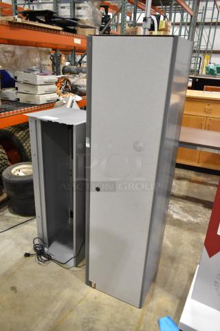 Two gray overhead cabinets for desks, vertical design, sturdy construction, minor wear. Includes power cord, ideal for office use.