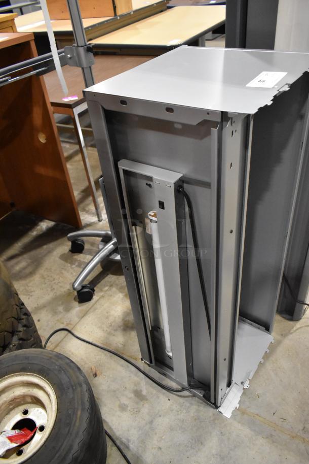 Gray overhead cabinet for desks, shown upright with visible wiring; auction label attached.