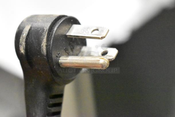 A close-up of a three-pronged electrical plug with a black casing, showing signs of wear and use.