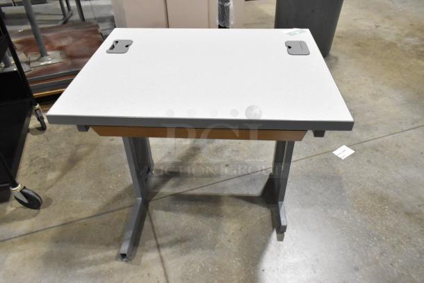 Gray desk with flat surface, metal legs, and cable slots. Durable condition. Includes a black 3-tier cart on casters.