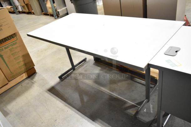 Modern office desk with a white tabletop and metal legs in good condition, shown in a warehouse setting.