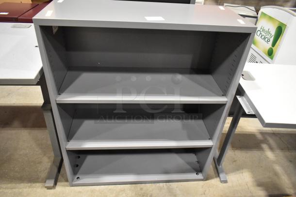 Gray metal bookshelf with three adjustable shelves, minimal wear, sturdy frame. Auction offers two identical pieces.