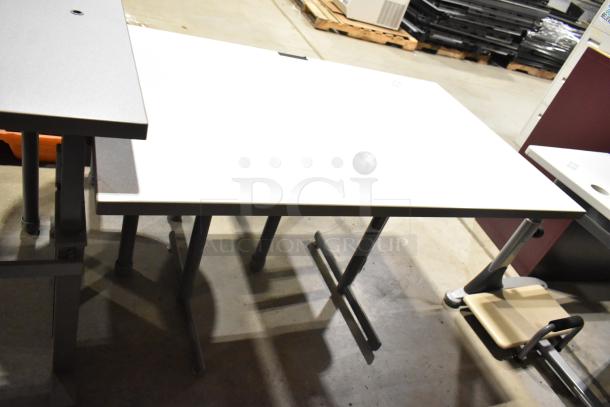 Three gray desks with metal legs, varying in size and condition, grouped together in an industrial setting.