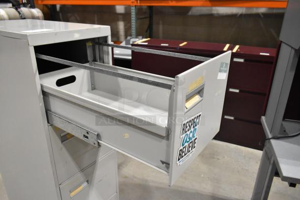 Gray metal 4-drawer filing cabinet with open top drawer. Visible sticker reads "Respect Ask Believe." Light wear visible.