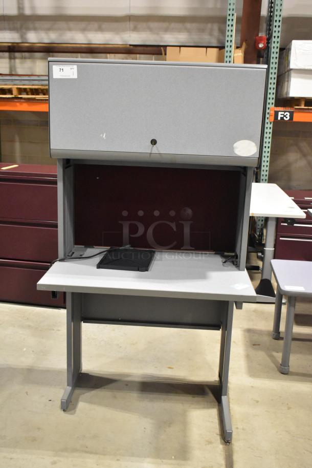 Gray desk with overhead cabinet, sturdy metal frame, in good condition. Features a lockable cabinet door and a flat workspace.