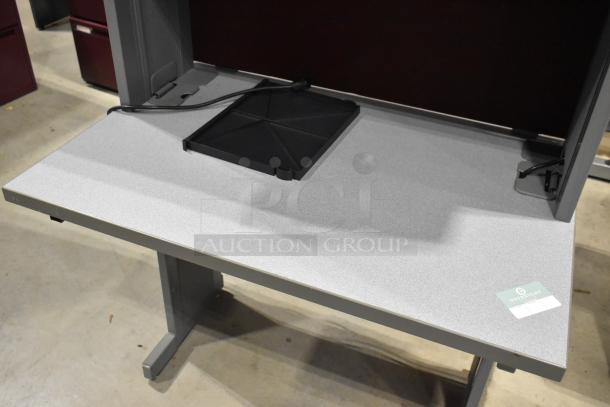 Gray desk with overhead cabinet, in good condition. Includes black cable management tray. Label on desk corner.