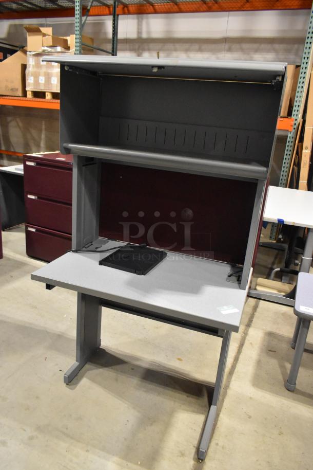 Gray desk with overhead cabinet; sturdy condition. Features pull-out shelf and cable cutout. Ideal for office use.