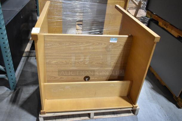 Wood-pattern desk with natural finish, flat-packed on a pallet. Features a cable management hole. Appears in good condition.