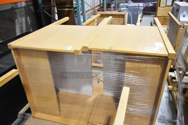 Two wood-pattern desks, wrapped in plastic, new condition, light wood finish, auction stickers visible on top surfaces.