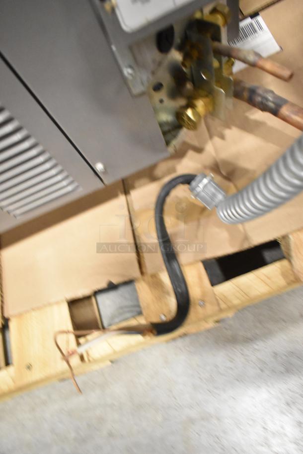 Rheem 13PJA24A01 air conditioner condenser, metal, 208/230V, 1 phase. Partial view of connections and mounting on pallet.