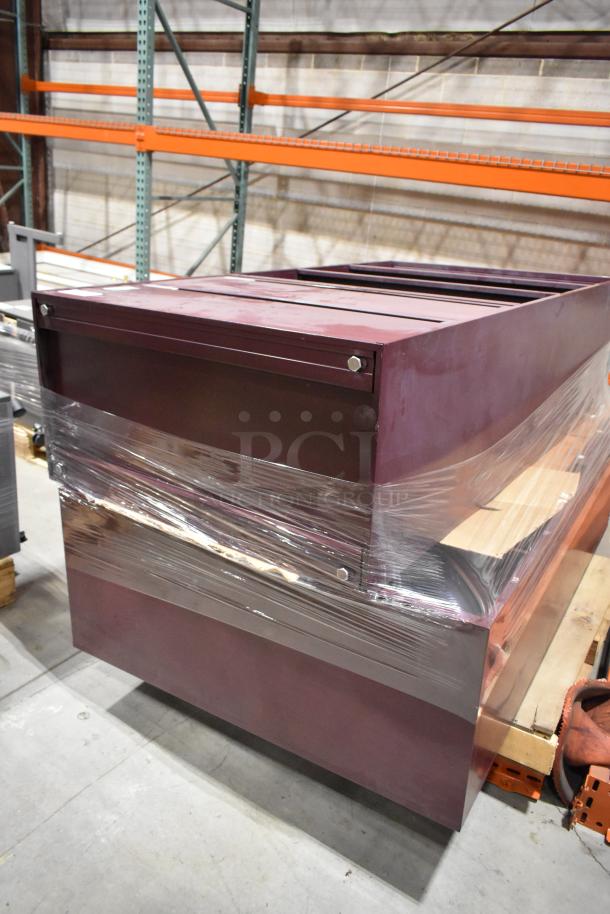 Two maroon metal cabinets, including one with two drawers, wrapped in plastic. Condition: Used.