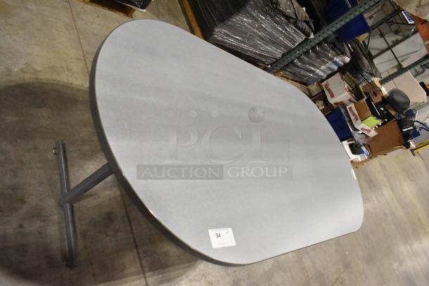 Gray oval table on a single metal pedestal base in a warehouse setting. Table marked with label "94". Condition appears good.